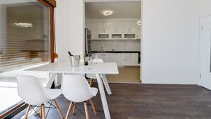 A modern kitchen with white cabinets, a white dining table, and a large window with blinds. - Dubrovnik Heights Luxury Villa (Ravno)