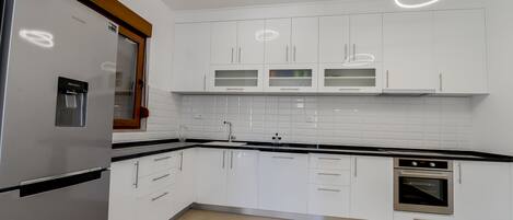 A modern kitchen with white cabinets, a stainless steel refrigerator, a built-in oven, and a water dispenser.