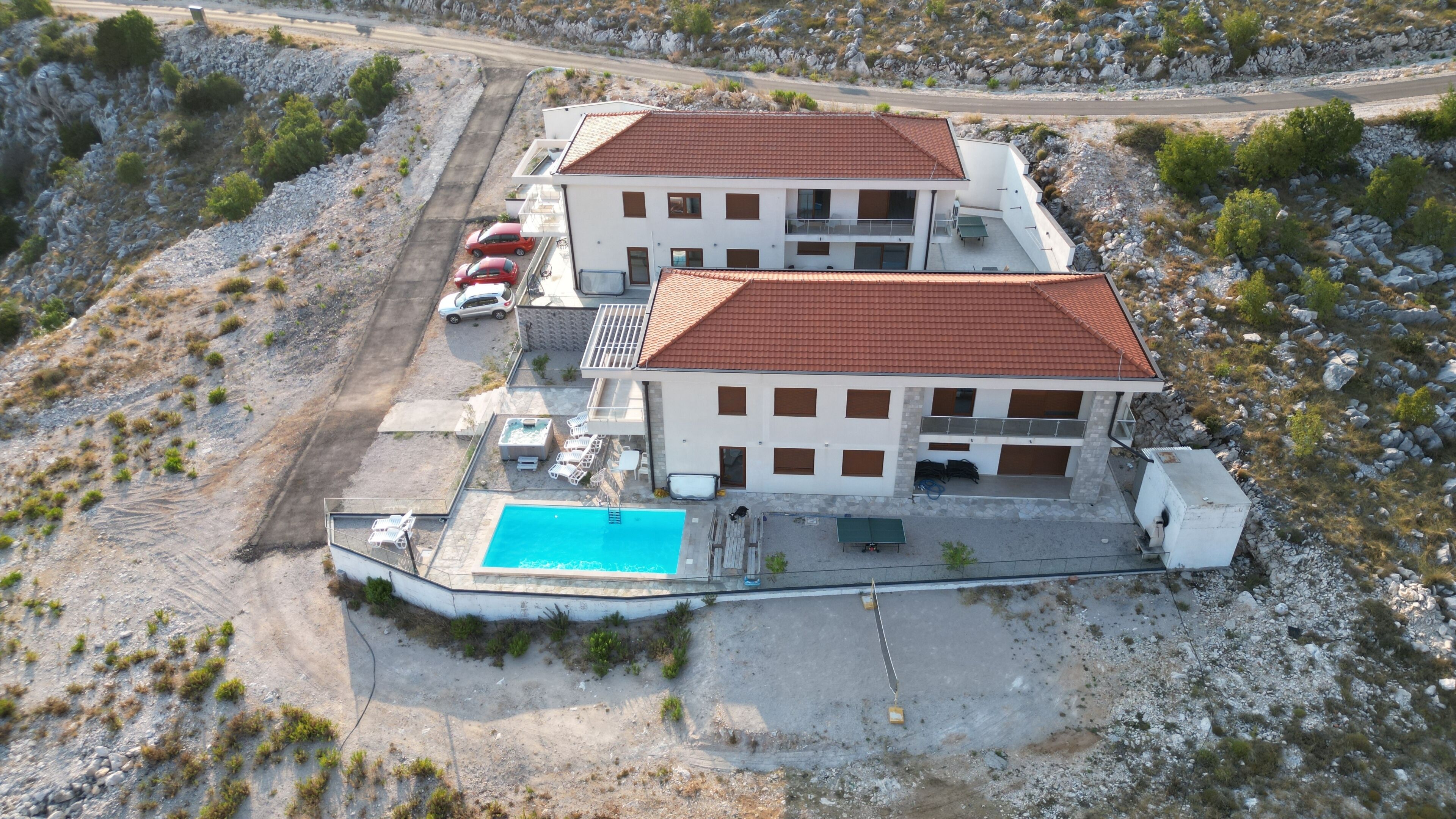 A two-story building with a swimming pool, a covered patio, and a parking area with two cars.