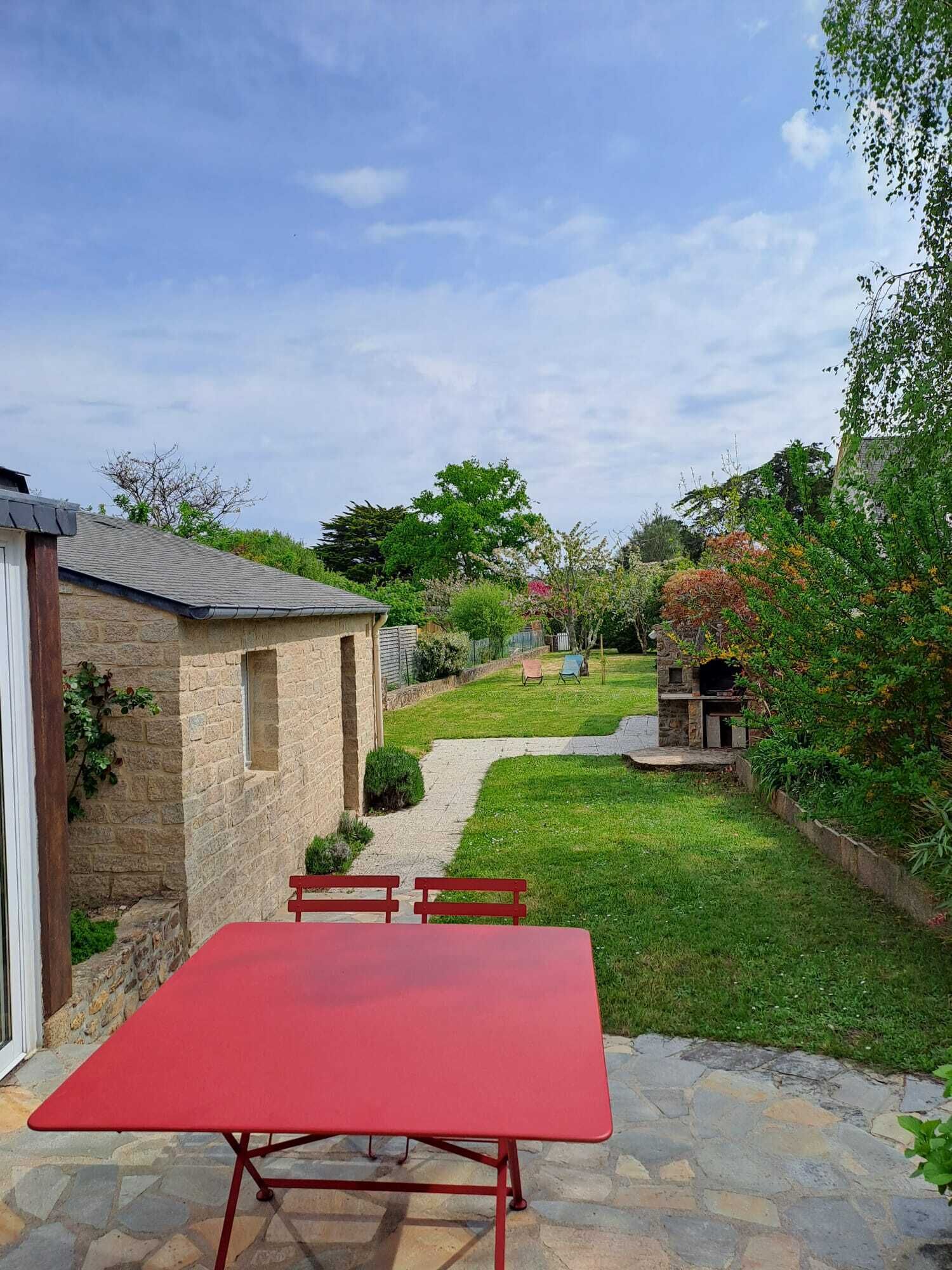 Un bâtiment en pierre avec une table et des chaises rouges dans un jardin.