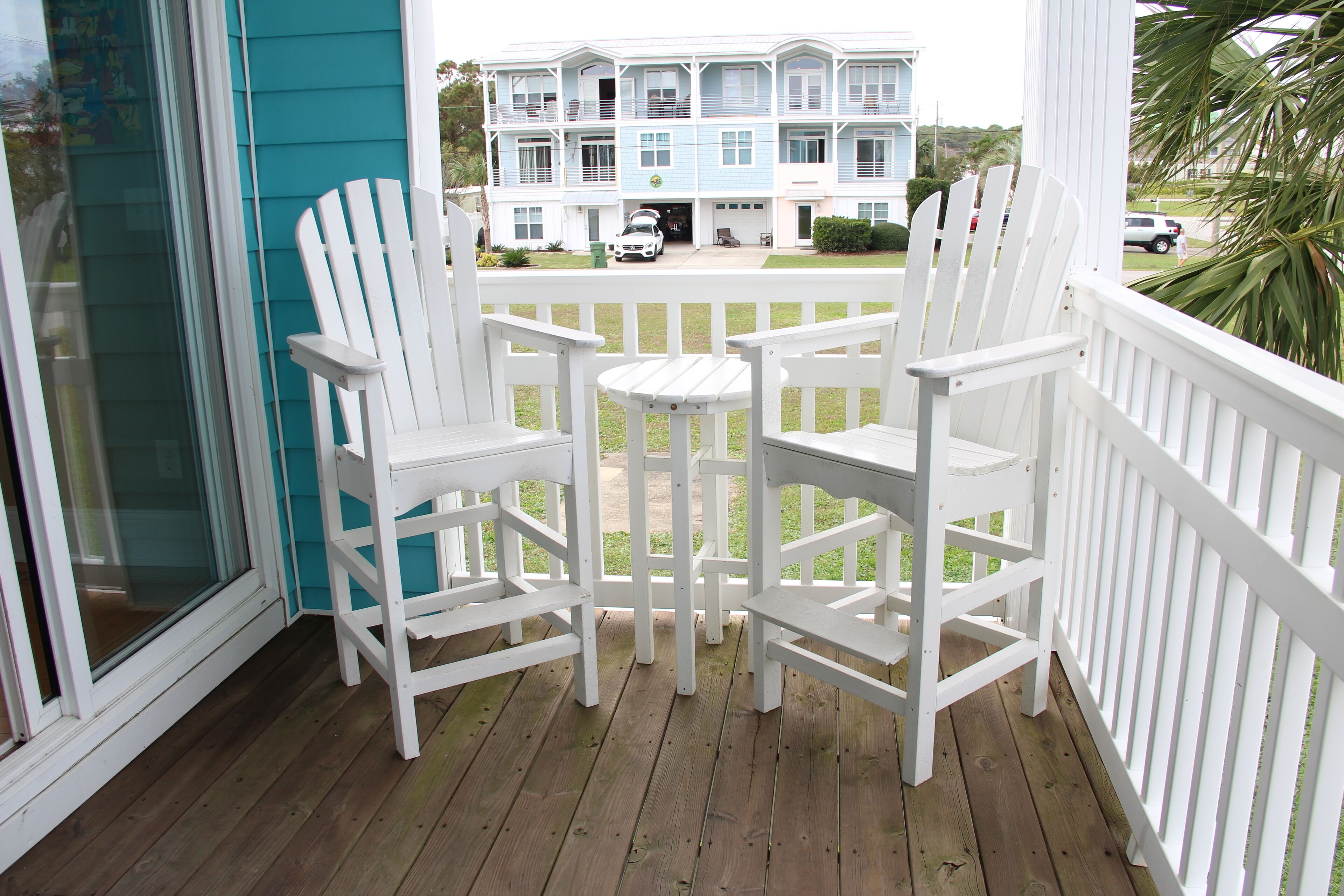 A wooden deck with white Adirondack chairs and a small table.