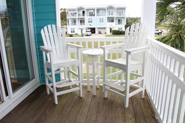 Una terraza de madera con sillas Adirondack blancas y una pequeña mesa.