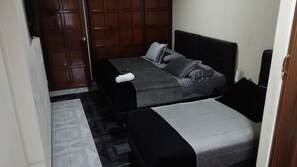 A small room with two beds, a wooden door, and a tiled floor.