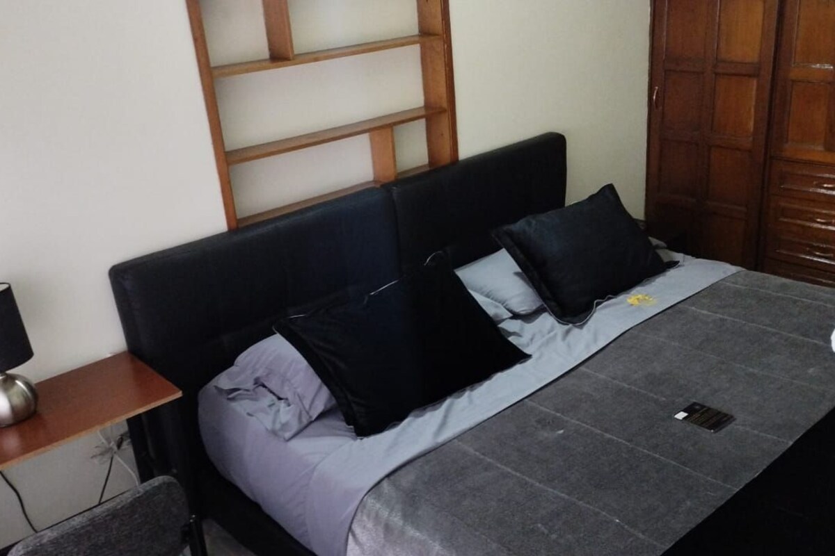 A bed with a dark headboard, a grey blanket, and two black pillows.