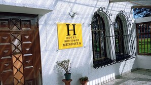 Un edificio con un cartel que dice 'HOTEL BOUTIQUE MENDOZA', una puerta de madera y tres ventanas de arco con rejas de metal.