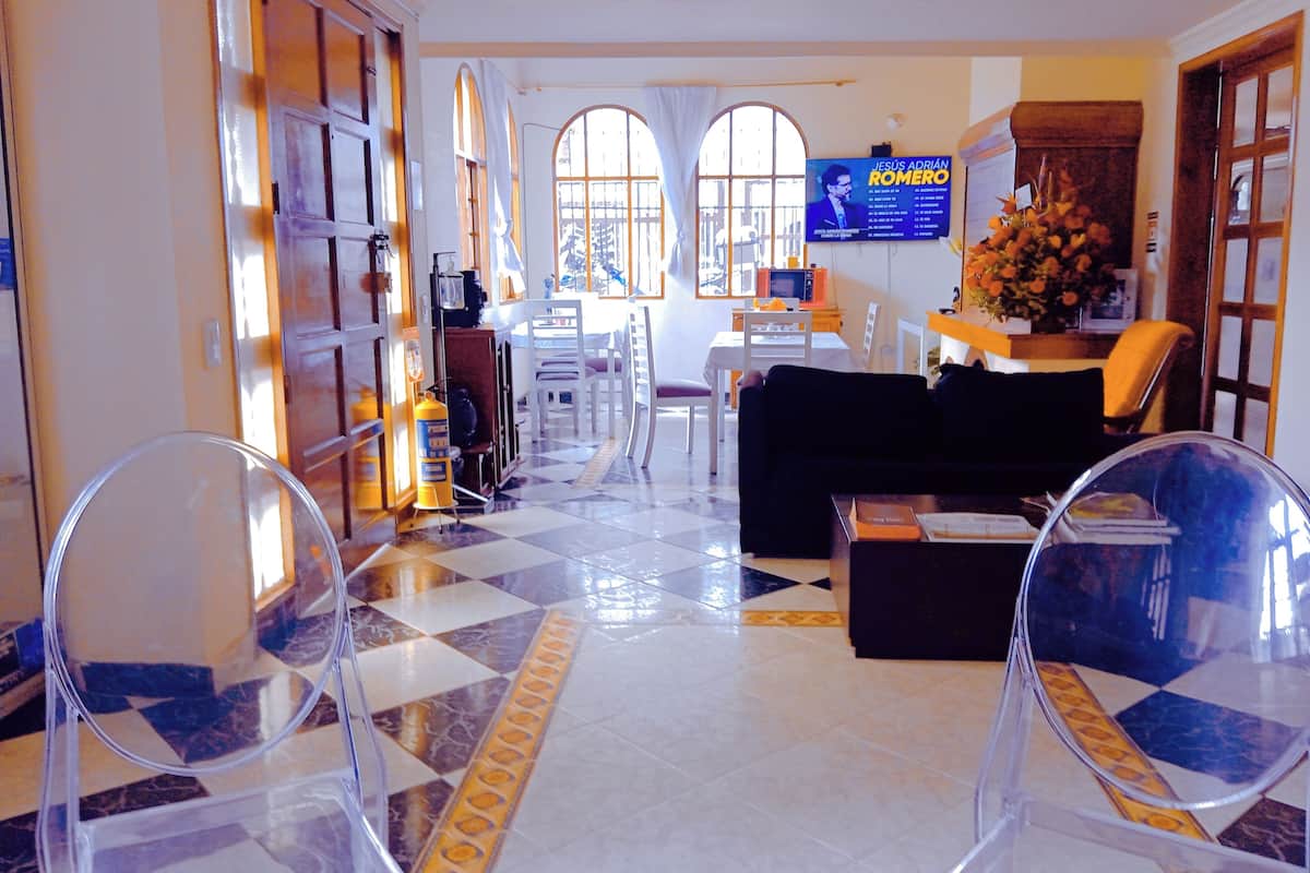 A hotel lobby with a checkered floor, a black sofa, a coffee table, and a TV displaying a movie poster.