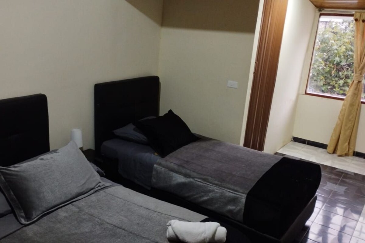 A room with two beds, a window with curtains, and a tiled floor.