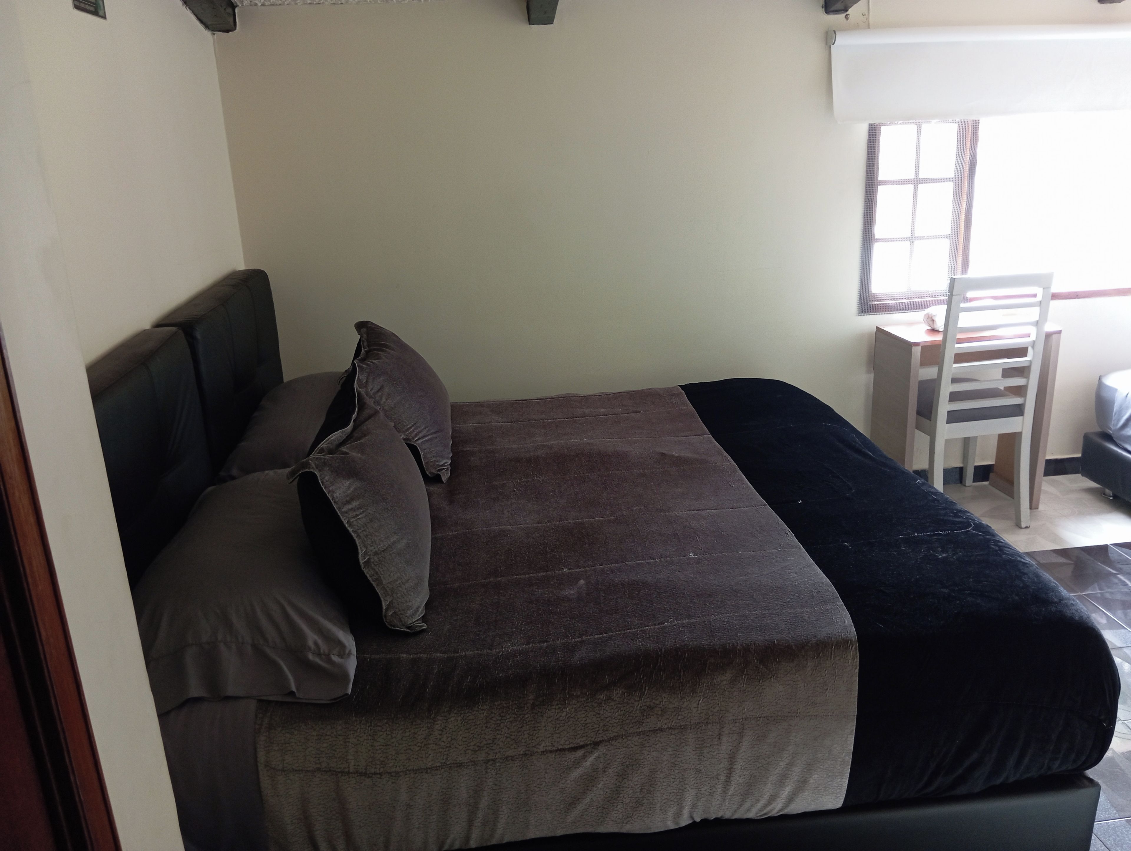 A single bed with a headboard, a desk, and a chair in a room with a window.