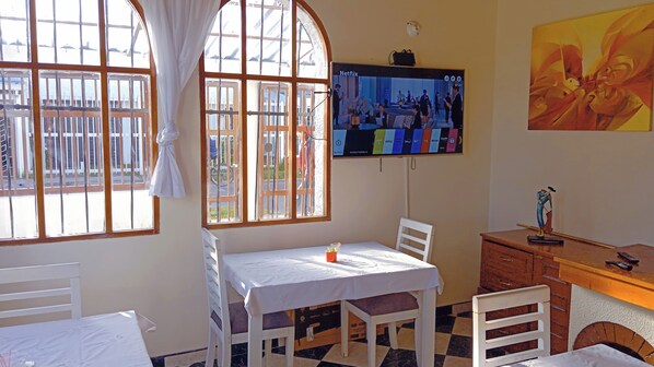 Une pièce avec un lit, une table sur laquelle se trouve une tasse, un téléviseur accroché au mur et une fenêtre avec des rideaux.