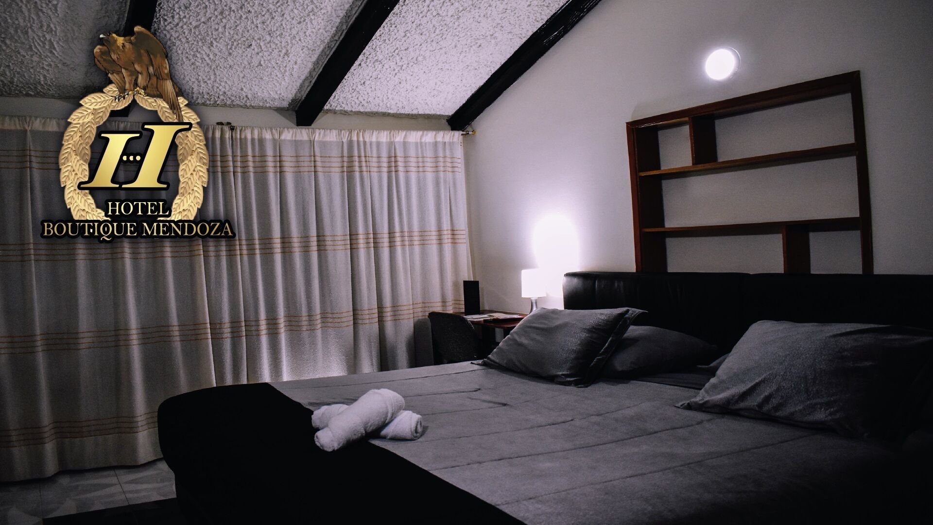 A hotel room with a bed, pillows, a nightstand, a lamp, and a window with curtains.