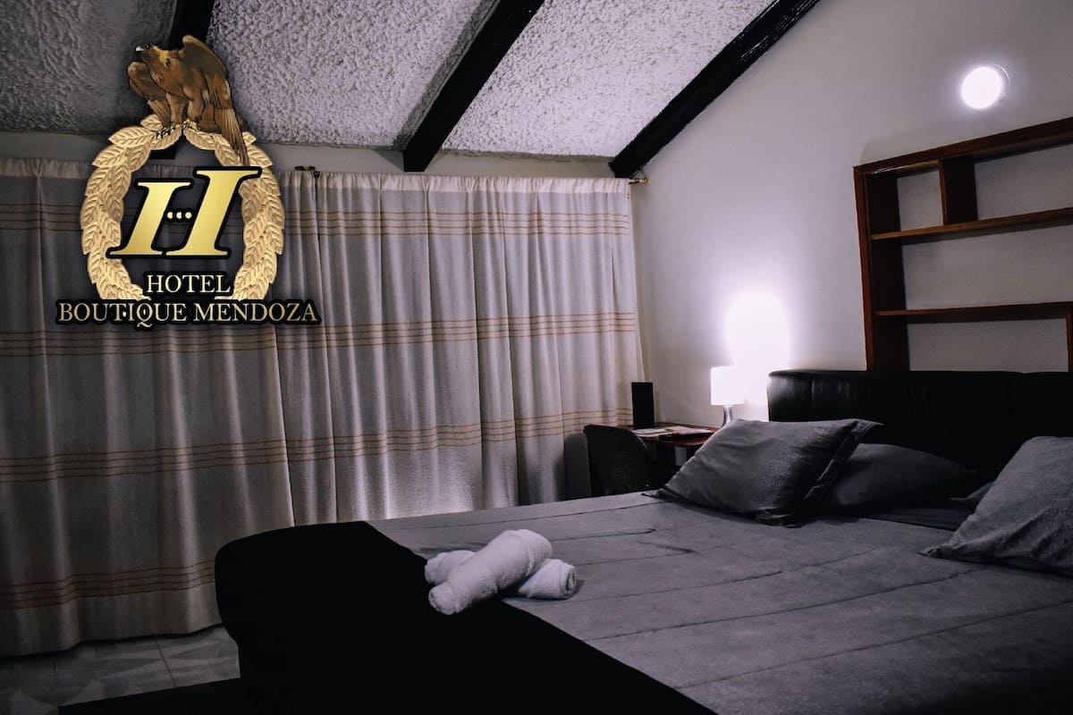 A hotel room with a bed, pillows, a nightstand, a lamp, and a window with curtains.