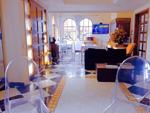 Un hall d’hôtel avec un sol à carreaux, un canapé noir, une table basse et un téléviseur diffusant une affiche de film.