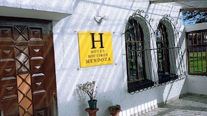 A building with a sign reading 'HOTEL BOUTIQUE MENDOZA,' a wooden door, and three arched windows with metal grilles. - Hotel Boutique Mendoza (Bogotá)