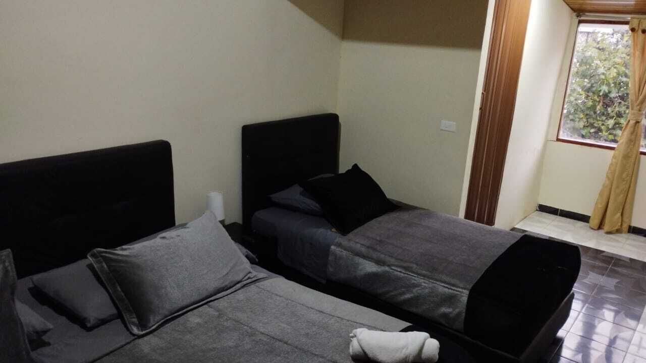 A room with two beds, a window with curtains, and a tiled floor.