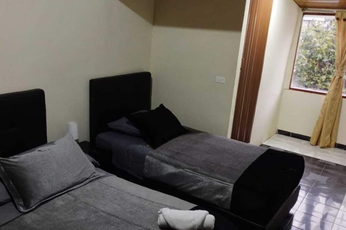 A room with two beds, a window with curtains, and a tiled floor.
