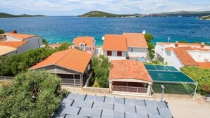 A coastal residential area with houses featuring red-tiled roofs, a clear view of the sea, and a hilly landscape in the background. - Apartment Marina by Interhome (Rogoznica/Ražanj)