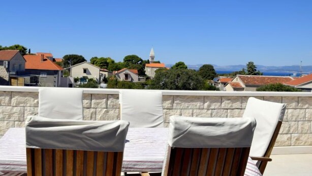 A terrace with two wooden chairs and a stone wall, overlooking a coastal town with houses and a church. - Margita by Interhome (Brač/Supetar)