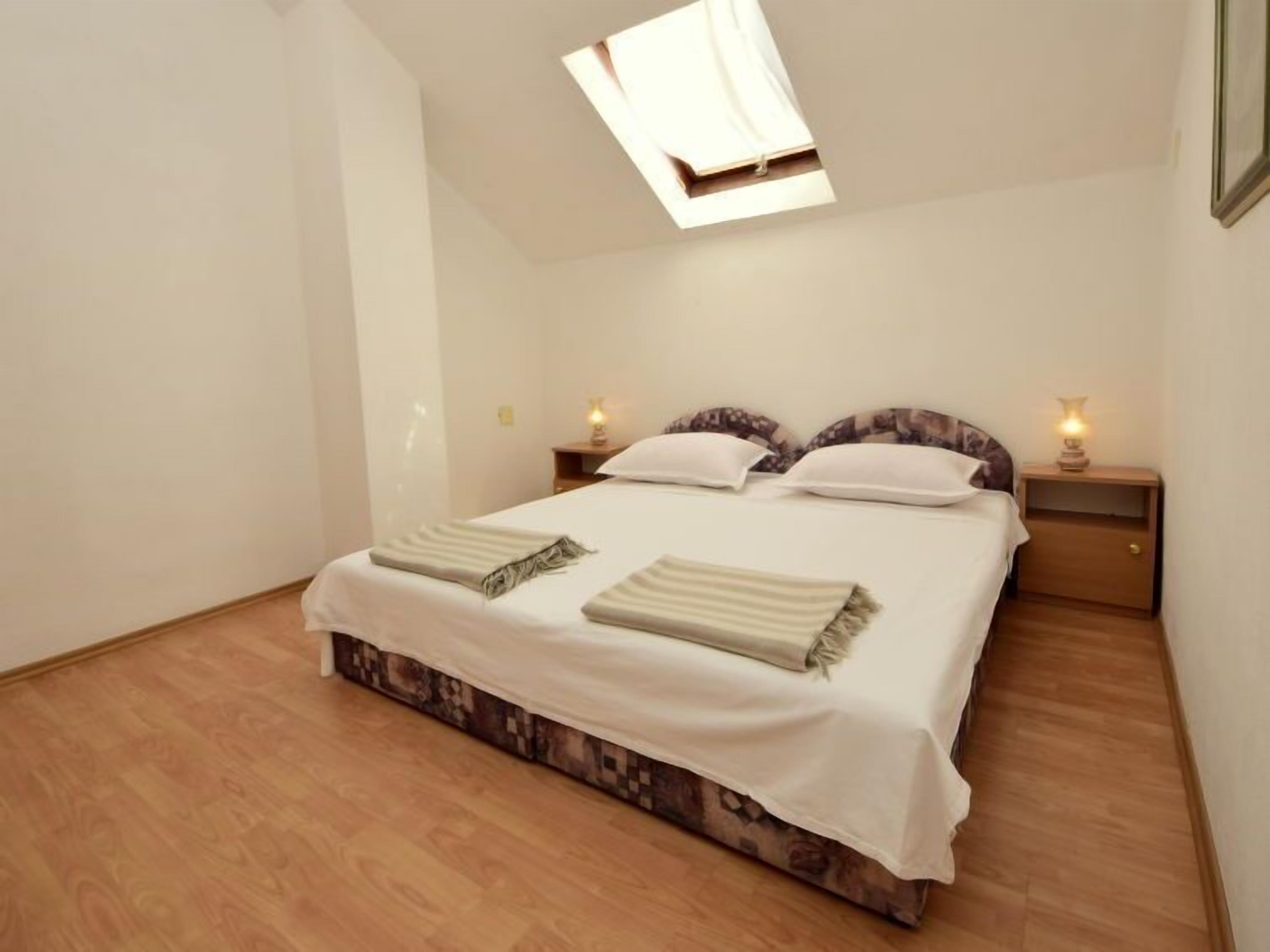 A bedroom with a bed, two bedside tables with lamps, a window, and a patterned carpet.