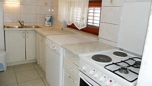 A compact kitchen with a sink, a washing machine, a stove, and a window with a lace curtain. - Margita by Interhome (Brač/Supetar)