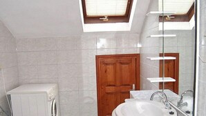 A small bathroom with a washing machine, a toilet, a sink with a mirror, and a skylight above. - Margita by Interhome (Brač/Supetar)