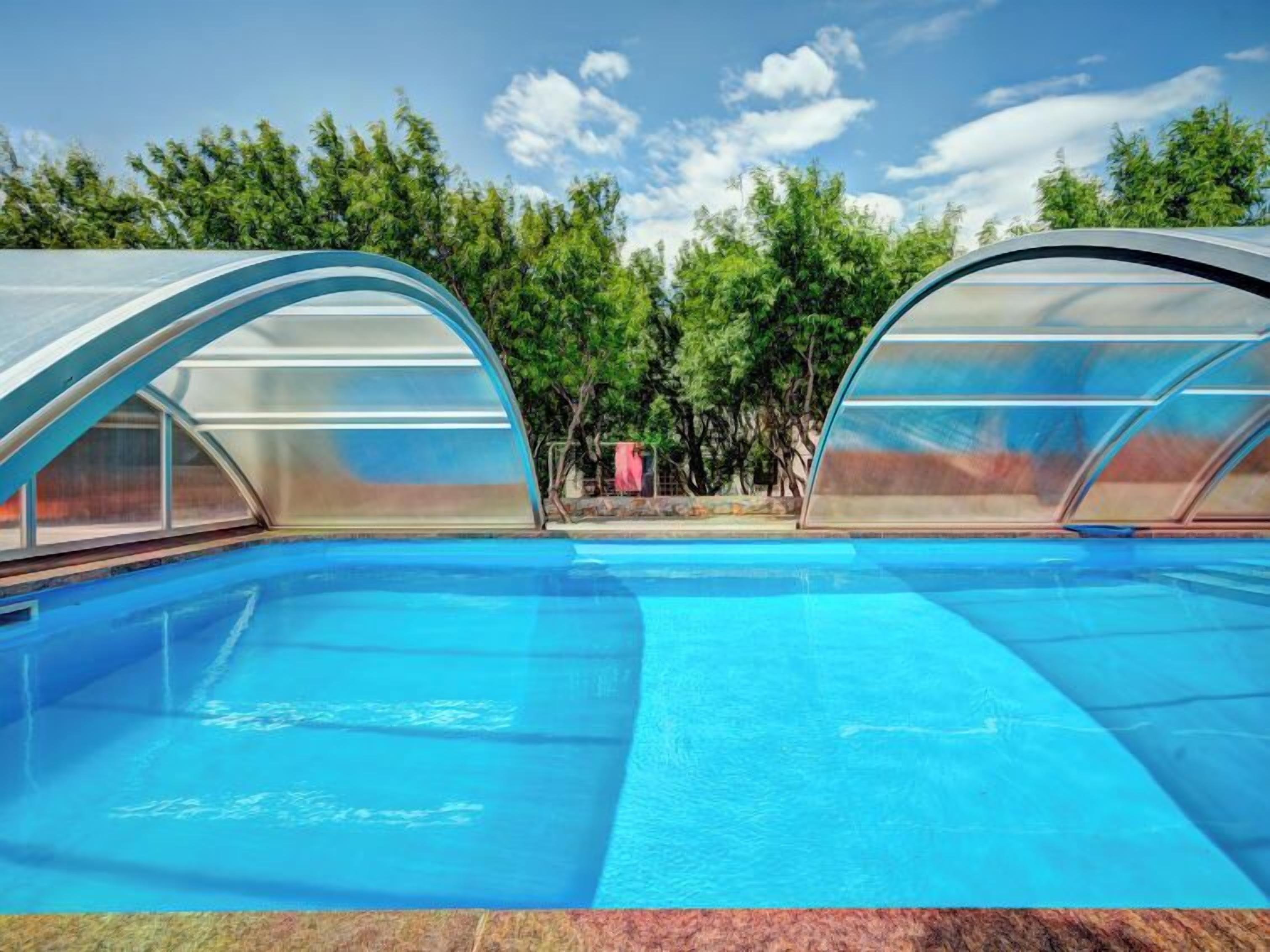 Une piscine dotée de deux zones abritées, entourée d’arbres et offrant une vue sur un ciel dégagé.