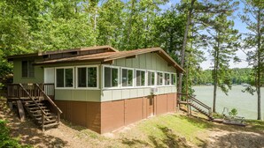 Eine Holzhütte mit einer Holzterrasse und einer Treppe zu einem überdachten Bereich, umgeben von Bäumen und einem See.