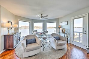 A spacious room with two armchairs, a dining table, and a view of a body of water through large windows. - Waterfront Hot Springs Condo: Pool, Hot Tub Access (Hot Springs)