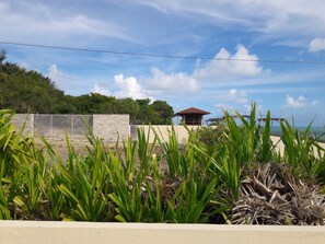 A coastal property with a stone wall, a small building with a tiled roof, and lush greenery in the foreground. - Pousada Laguna (Conde)