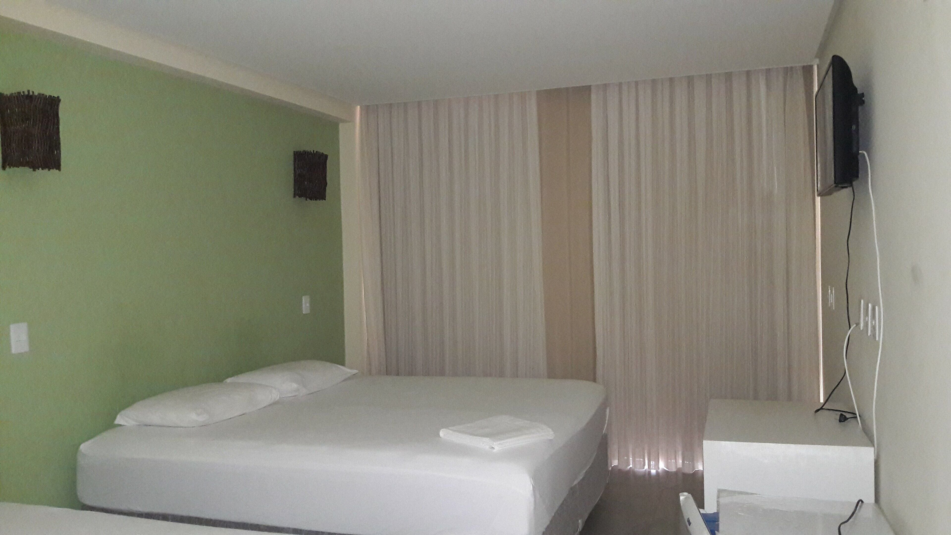 A hotel room with a single bed, a small bedside table, and a television mounted on the wall.