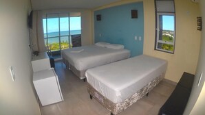 A room with two beds, a small desk, and a view of the sea. - Pousada Laguna (Conde)