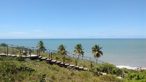 A coastal view with a staircase leading down to the beach, palm trees, and the ocean. - Pousada Laguna (Conde)