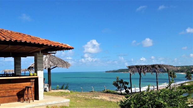 A beachside bar with a tiled roof and thatched umbrellas, overlooking a clear blue sea and a distant island. - Pousada Laguna (Conde)