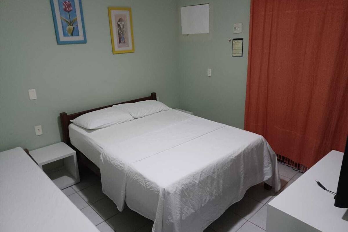 A bedroom with a single bed, a bedside table, a small stool, and a desk with a chair.