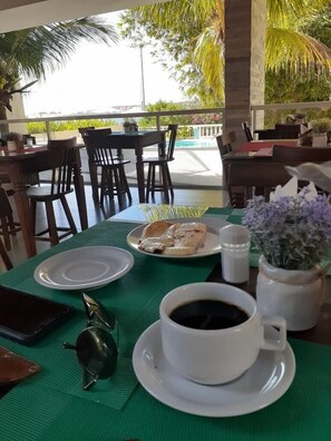 A dining area with tables set for two, featuring a green tablecloth, a plate with food, a cup of coffee, and a salt shaker. - Pousada Laguna (Conde)