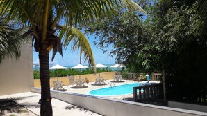 A swimming pool with white chairs and umbrellas, surrounded by greenery and a view of the sea. - Pousada Laguna (Conde)