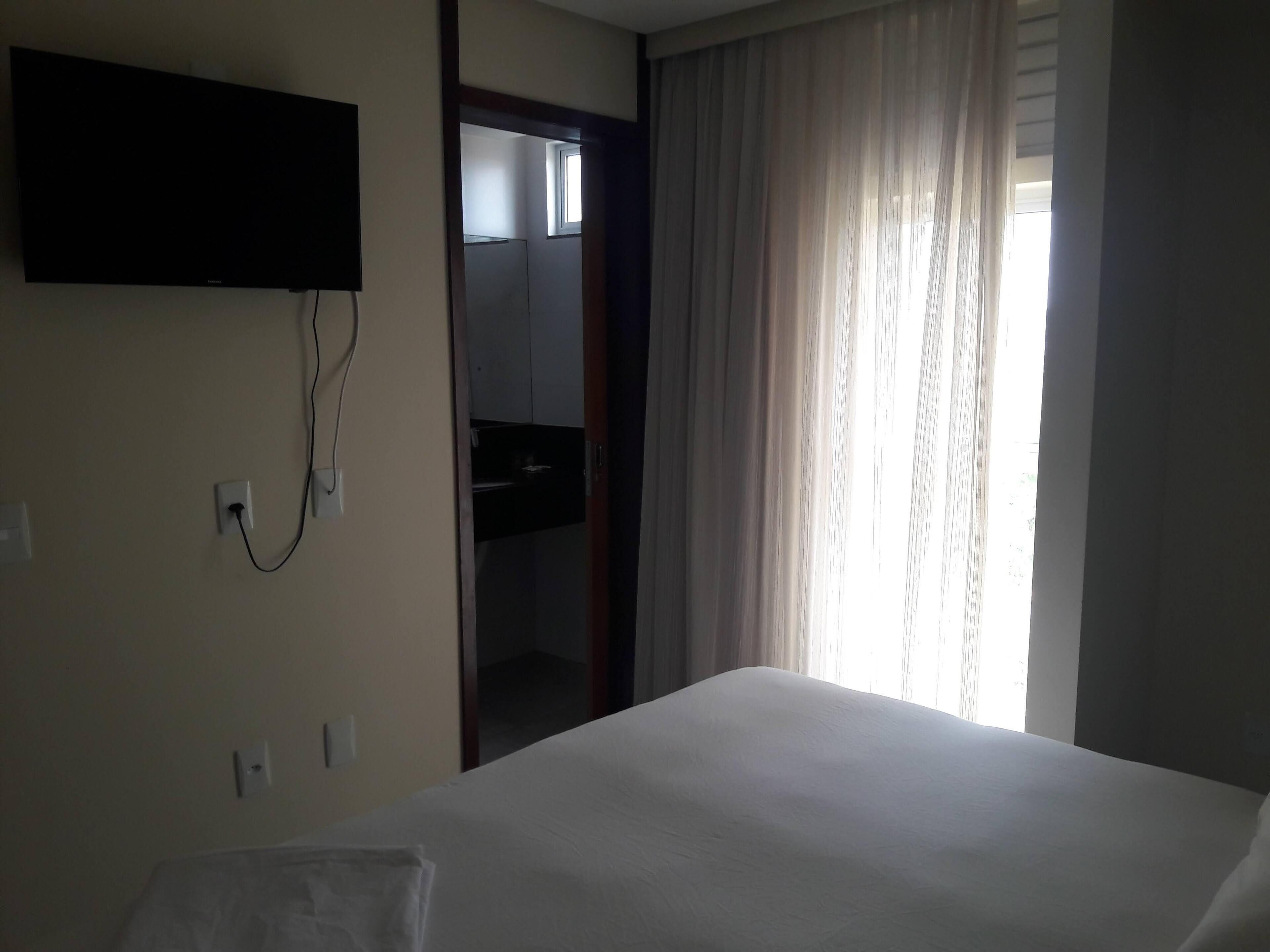 Una habitación de hotel con una cama, un televisor montado en la pared y una ventana con cortinas.