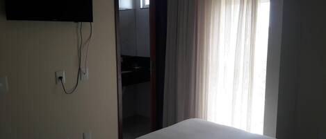 Una habitación de hotel con una cama, un televisor montado en la pared y una ventana con cortinas.