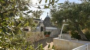 A stone building with a conical roof, surrounded by olive trees and a stone wall. - Stylish Trulli with Private Pool for 4 guests in Puglia (Castellana Grotte)