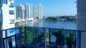 A balcony with a view of a body of water, tall buildings, and a distant structure. - Across from the Beach Edificio El Nuevo Conquistador Apto 612 Barrio El Laguito (Cartagena)
