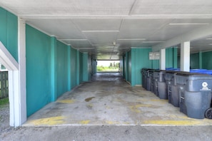 A covered parking area with teal walls and a row of black trash bins on the right.