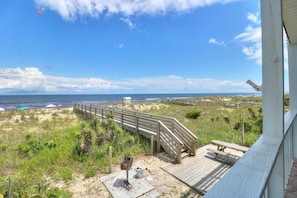 A beach view with a wooden boardwalk, a barbecue grill, and a beach umbrella.