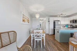 A modern kitchen with white cabinets, a central island, and a dining area with a wooden table and chairs.