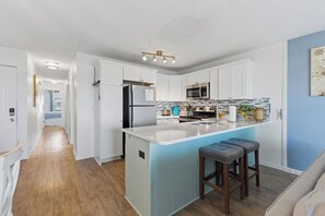 A modern kitchen with white cabinets, a blue island, stainless steel appliances, and a bar stool.