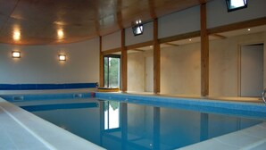 Una piscina interior con agua azul cristalina, vigas de madera y un borde de baldosas.
