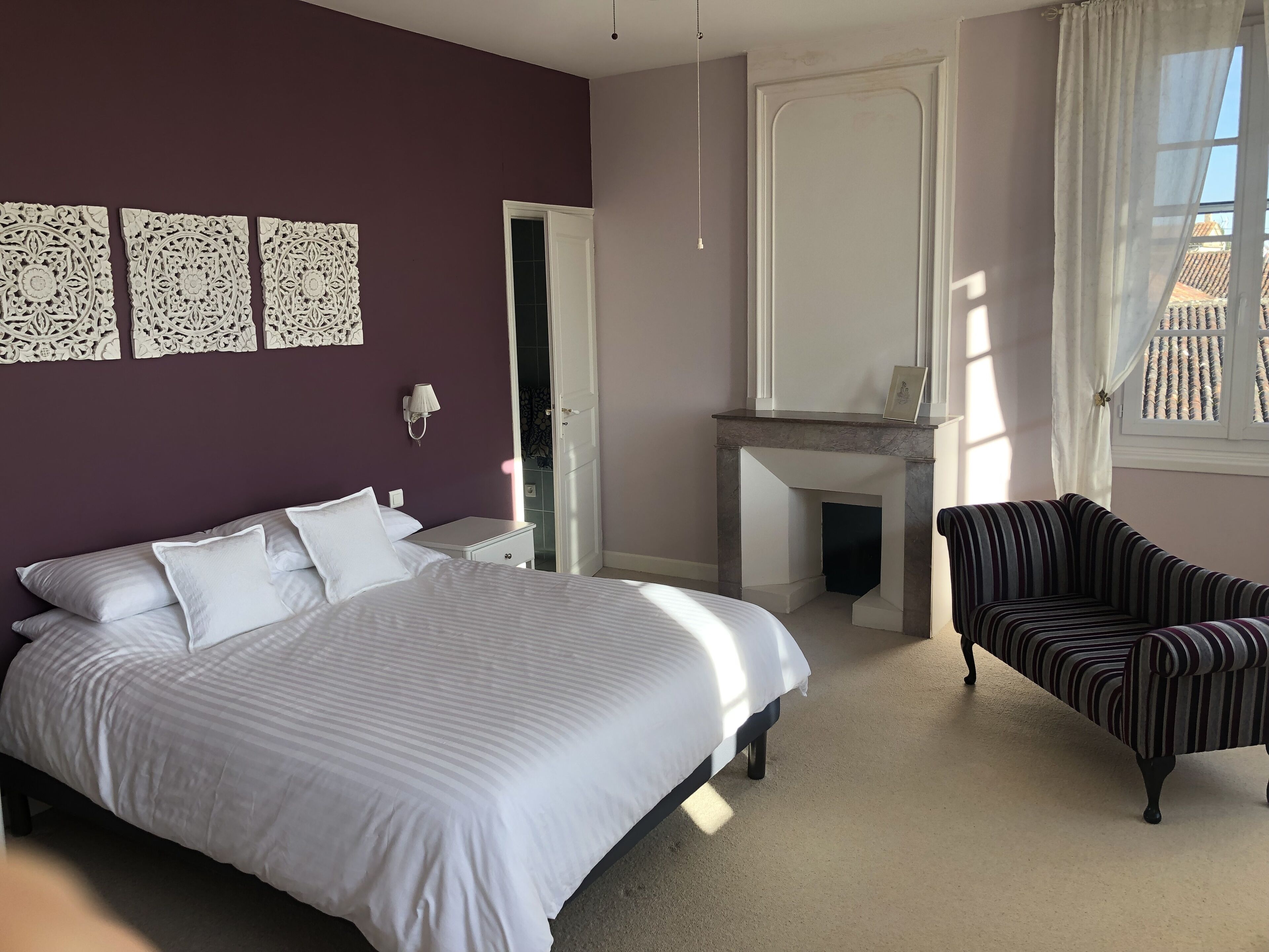 Ein Schlafzimmer mit einem Bett, einem Sessel, einem Kamin und Wandbildern.