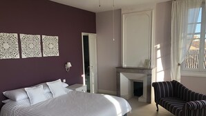 Un dormitorio con cama, una silla, chimenea y decoración en la pared.
