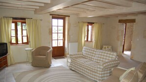 Una sala de estar con un sofá color beige, un sillón pequeño, un televisor y una alfombra estampada.