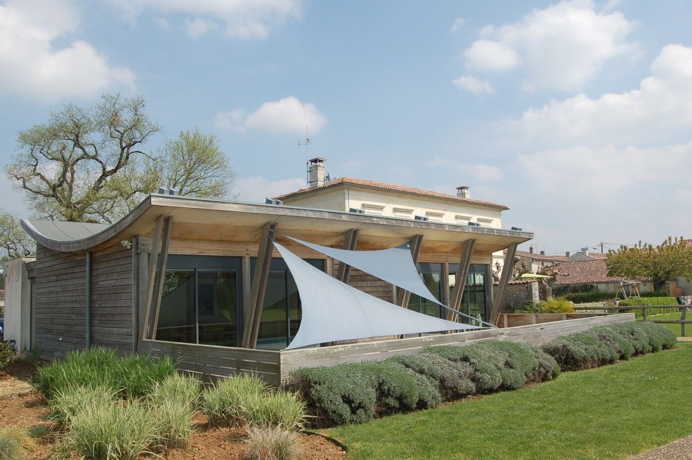 Une maison moderne dotée d’un toit au design original, de grandes fenêtres et d ’un jardin bien entretenu.