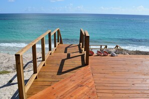 Una terraza de madera que da a una playa con agua azul cristalina y orilla arenosa.