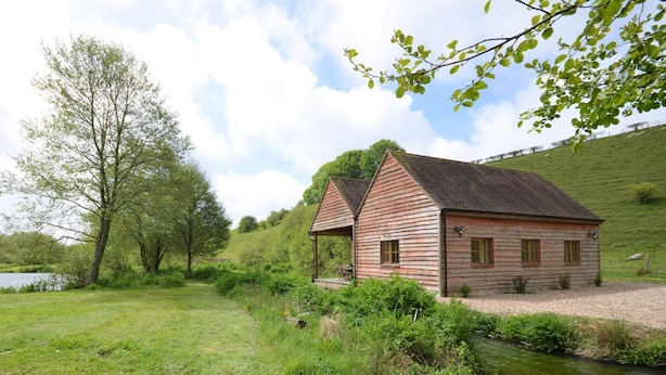 A rustic wooden cabin with a sloped roof, situated beside a small stream.